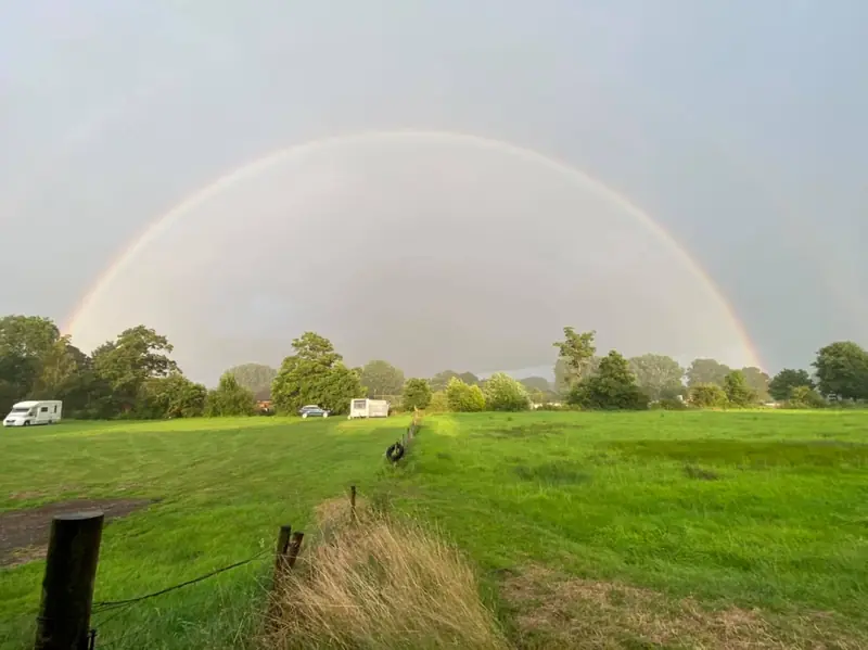 A full rainbow arching over Bridge Meadow with caravans in the distance